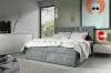 Elegantes graues Boxspringbett mit hohem Kopfteil vor hellem Hintergrund im Schlafzimmer.