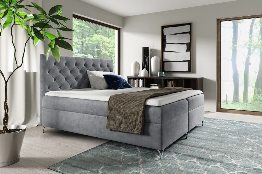 Graues Boxspringbett mit Chesterfield-Kopfteil und eleganten Metallfüßen im hellen Raum.