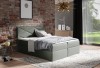 Graugrünes Boxspringbett mit geometrischem Kopfteil-Design vor einer Backsteinwand.