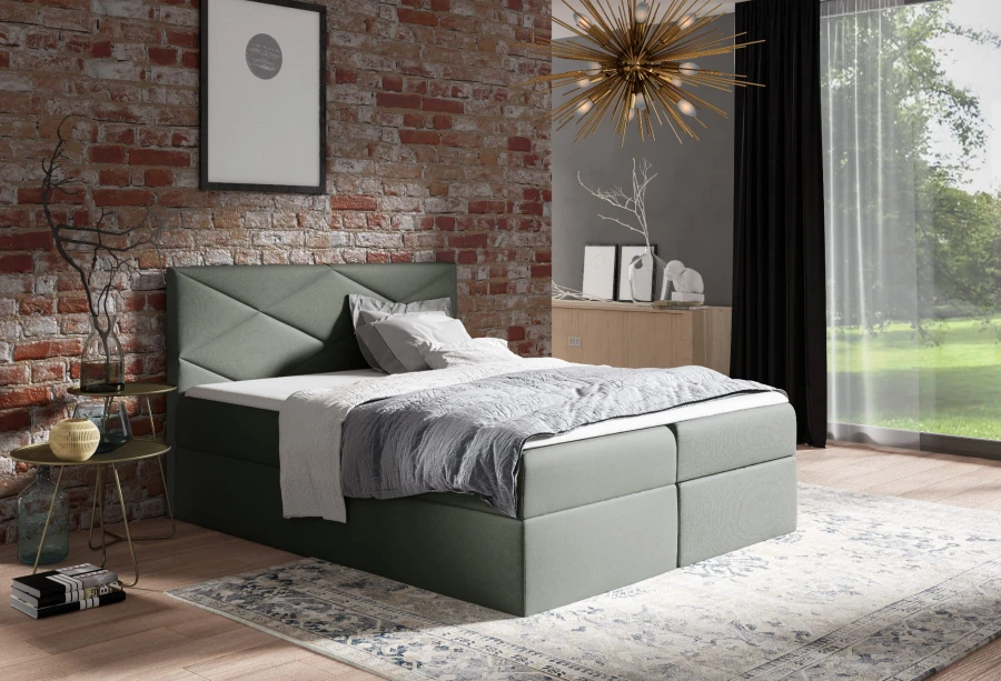 Graugrünes Boxspringbett mit geometrischem Kopfteil-Design vor einer Backsteinwand.