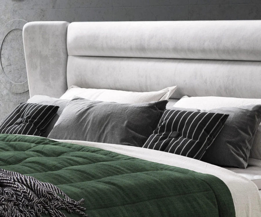Detailaufnahme der Kissen und des weich gepolsterten Kopfteils eines grauen Boxspringbetts.