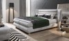 Modernes Boxspringbett in Hellgrau mit grünem Plaid und Dekokissen.