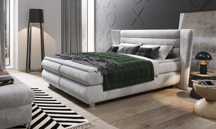 Modernes Boxspringbett in Hellgrau mit grünem Plaid und Dekokissen.