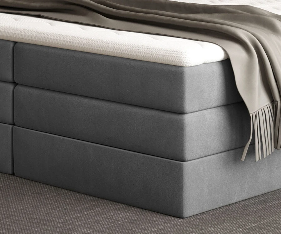 Detailansicht der grauen gepolsterten Basis eines Boxspringbettes mit Matratze.