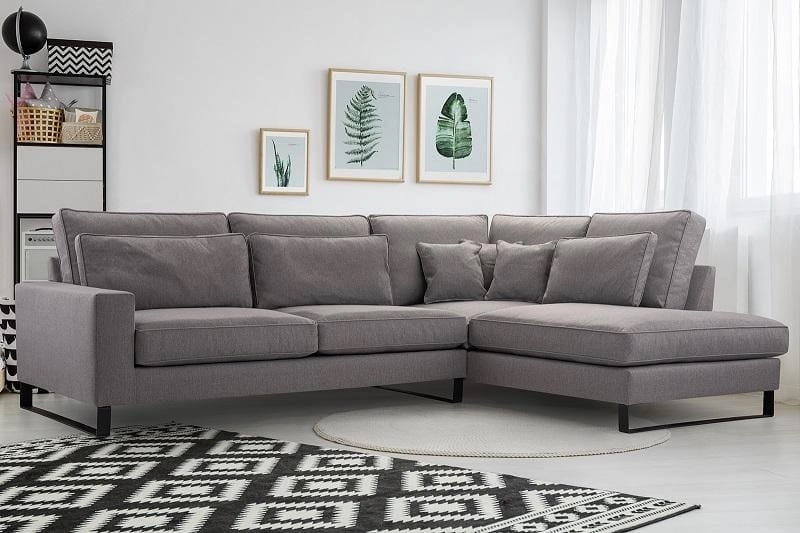 Modernes graues Ecksofa in einem hellen Wohnzimmer mit geometrischem Teppich.