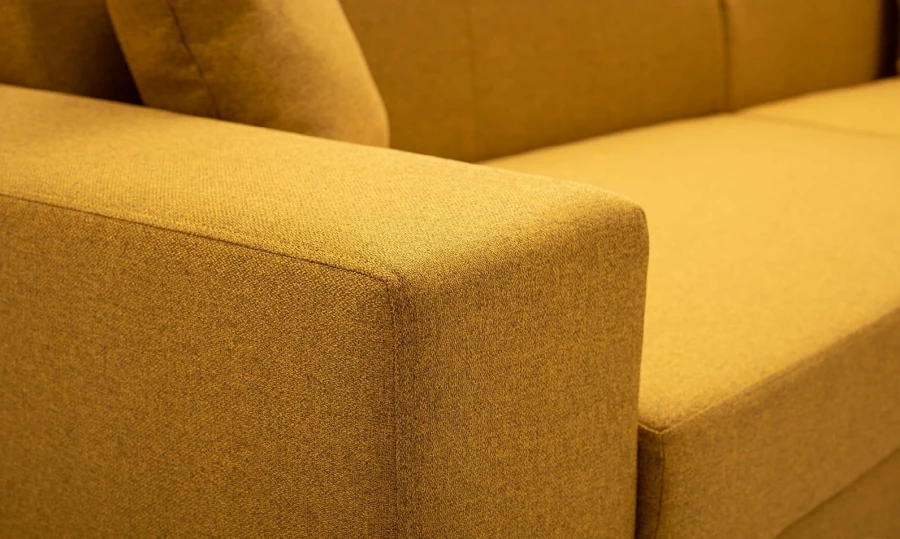 Detailansicht der hochwertigen Stoffstruktur und Armlehne eines modernen gelben Sofas.