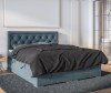 Blaues Polsterbett mit gestepptem Kopfteil und grauer Bettwäsche in modernem Schlafzimmer.