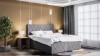 Eingerichtetes Schlafzimmer mit grauem Boxspringbett, Teppich und moderner Zimmerbeleuchtung.