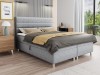 Hellgraues Boxspringbett mit gepolstertem Kopfteil im Schlafzimmer-Ambiente.