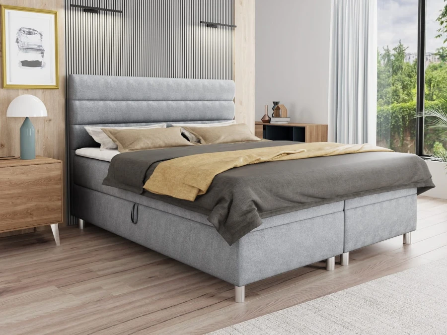 Hellgraues Boxspringbett mit gepolstertem Kopfteil im Schlafzimmer-Ambiente.