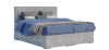 Freistehendes graues Boxspringbett mit gestepptem Kopfteil und blauer Bettdecke auf weißem Grund.