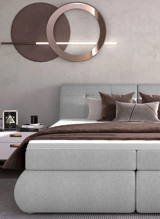 Modernes graues Boxspringbett mit braunen Kissen in einem stilvoll eingerichteten Schlafzimmer.