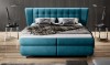 Frontansicht eines türkisen Boxspringbetts mit hohem Kopfteil und Designerlampen.