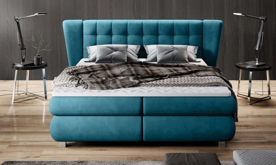 Frontansicht eines türkisen Boxspringbetts mit hohem Kopfteil und Designerlampen.