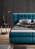 Modernes Boxspringbett in Petrol im Schlafzimmer mit dunkler Holzwand und stylischer Nachttischlampe.