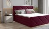 Bordeauxrotes Boxspringbett mit Rautenmuster-Polsterung in einem hellen Schlafzimmer.