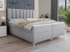 Hellgraues Boxspringbett mit hohem, vertikal gestepptem Kopfteil.
