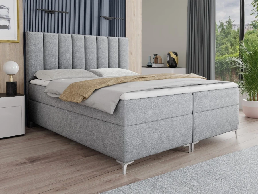 Hellgraues Boxspringbett mit hohem, vertikal gestepptem Kopfteil.