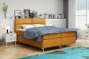 Senfgelbes Boxspringbett im hellen Schlafzimmer mit blauem Teppich und Deko.
