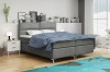 Graues Boxspringbett mit blauer Tagesdecke im hellen, modernen Schlafzimmer.