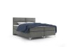 Graues Polsterbett Boxspring Design mit blauer Decke auf weißem Grund.