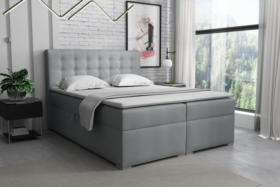 Graues Boxspringbett mit gepolstertem Kopfteil in hellem Raumambiente.