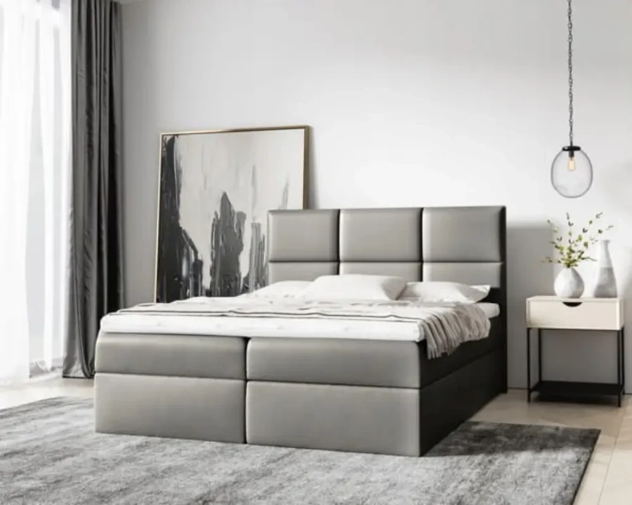 Graues Boxspringbett mit gepolstertem Kopfteil in einem hellen, modernen Schlafzimmer.