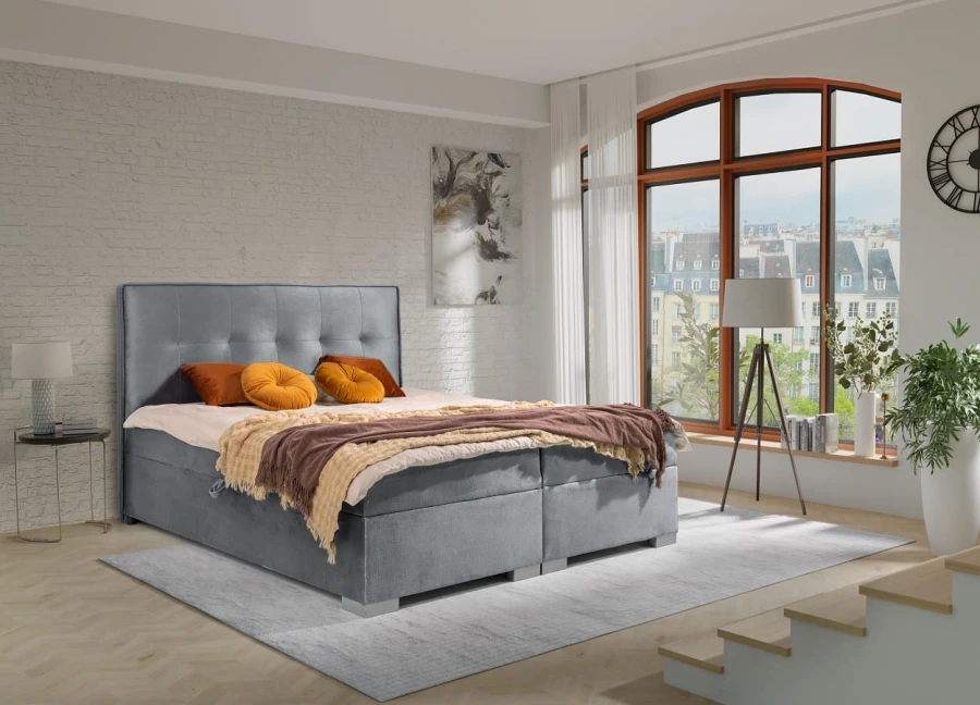 Hellgraues Boxspringbett in modernem Schlafzimmer mit Stadtblick und gemütlicher Deko.