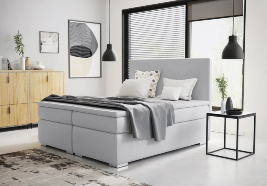 Minimalistisches weißes Boxspring-Doppelbett mit grauer Decke in hellem Raum.