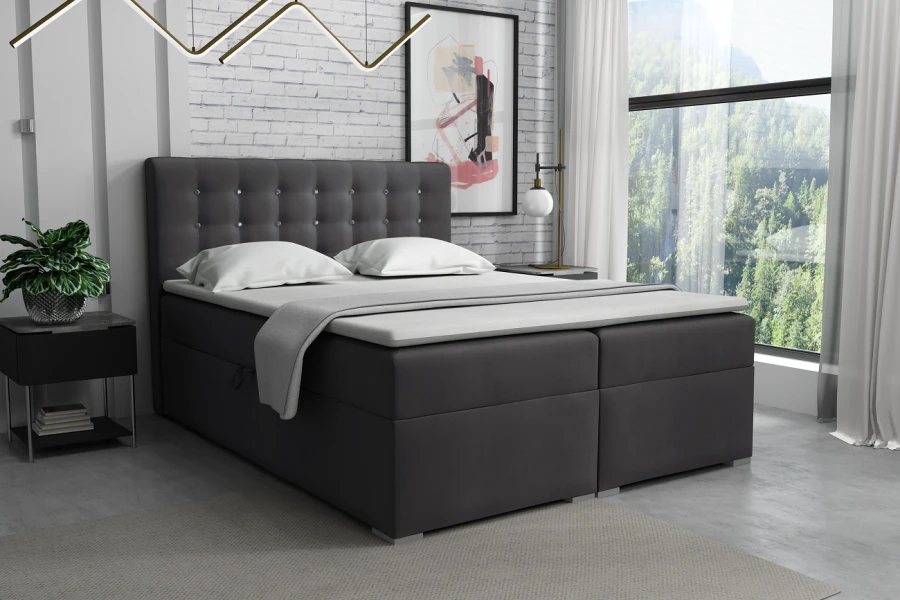 Dunkelgraues Boxspringbett inklusive Topper und dekorativem Kopfteil vor Backsteinwand.