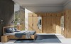 Modernes Schlafzimmer-Set in Eiche mit großem Eckschrank-System, Bett und blauem Teppich.