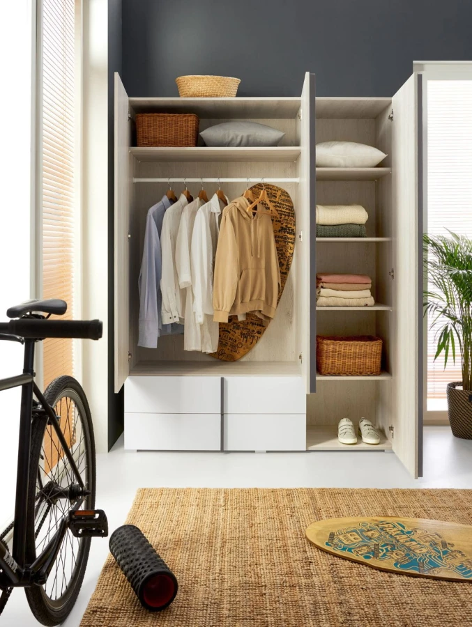 Eingerichteter Kleiderschrank mit Kleidung und Accessoires in einem hellen Zimmer mit Fahrrad.