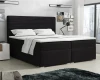 Elegantes schwarzes Boxspringbett mit gepolstertem Kopfteil und weißer Bettwäsche.