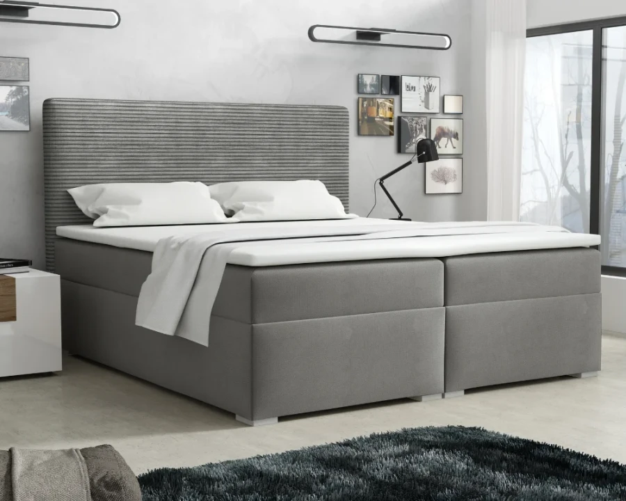 Graues Boxspringbett mit markantem Rillen-Kopfteil in einem hellen Schlafzimmer-Ambiente.