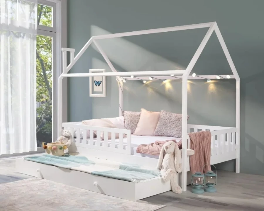 Weißes Hausbett für Kinder mit Ausziehbett, gemütlich dekoriert mit Lichterkette und Kissen im Kinderzimmer.