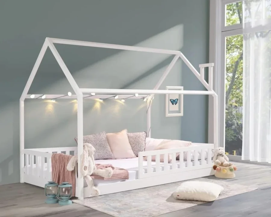 White children's house bed with fall protection and fairy lights in a cosy atmosphere.