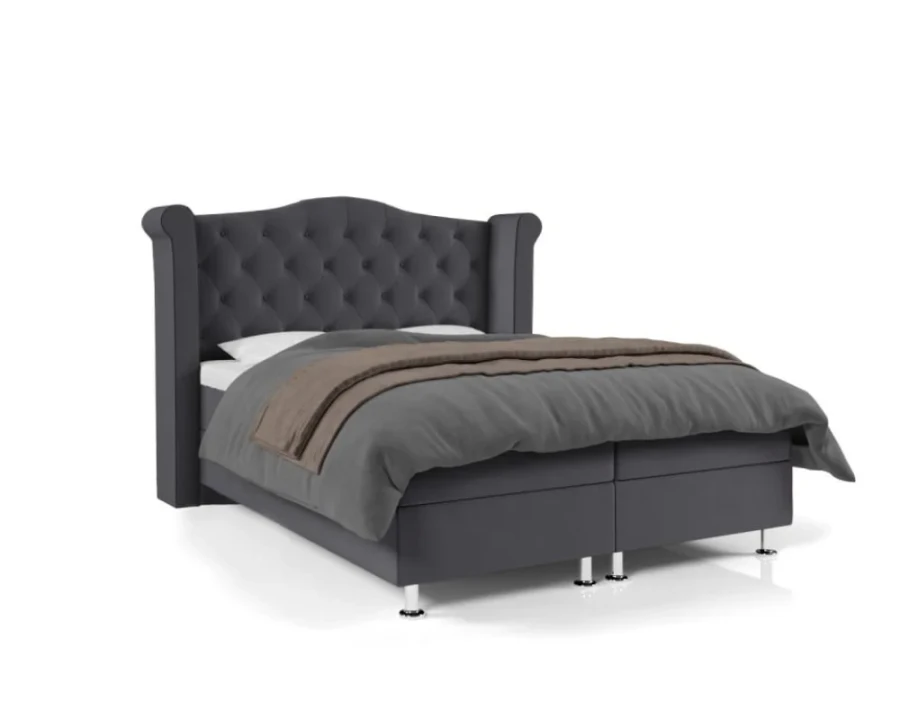 Graues Boxspringbett mit gestepptem Kopfteil und modernen Chromfüßen vor weißem Hintergrund.