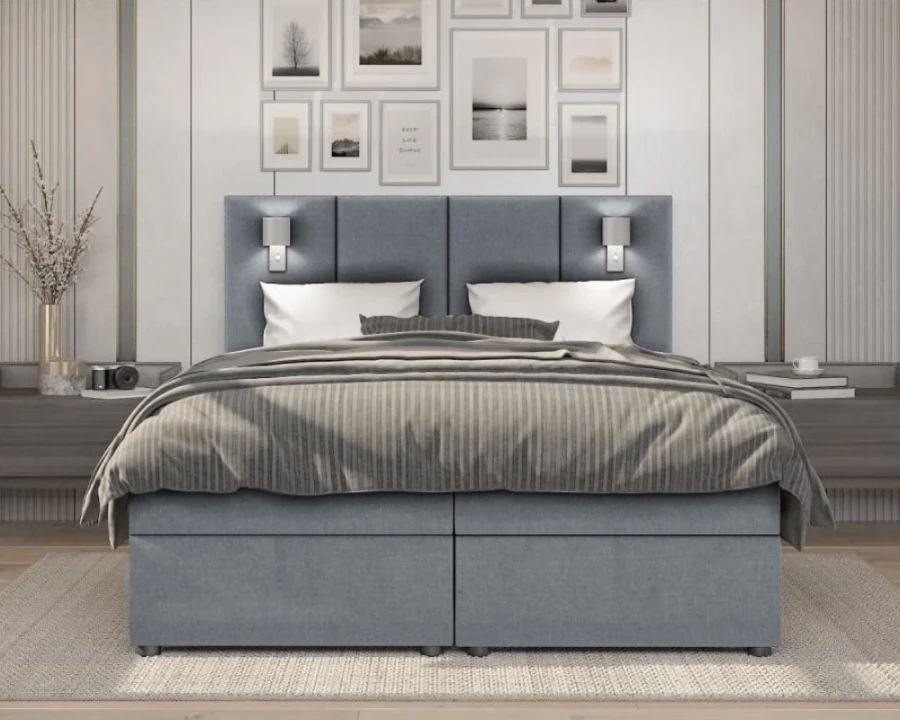 Frontalansicht eines hellblauen Boxspringbetts mit hohem Kopfteil und integrierten Lampen.