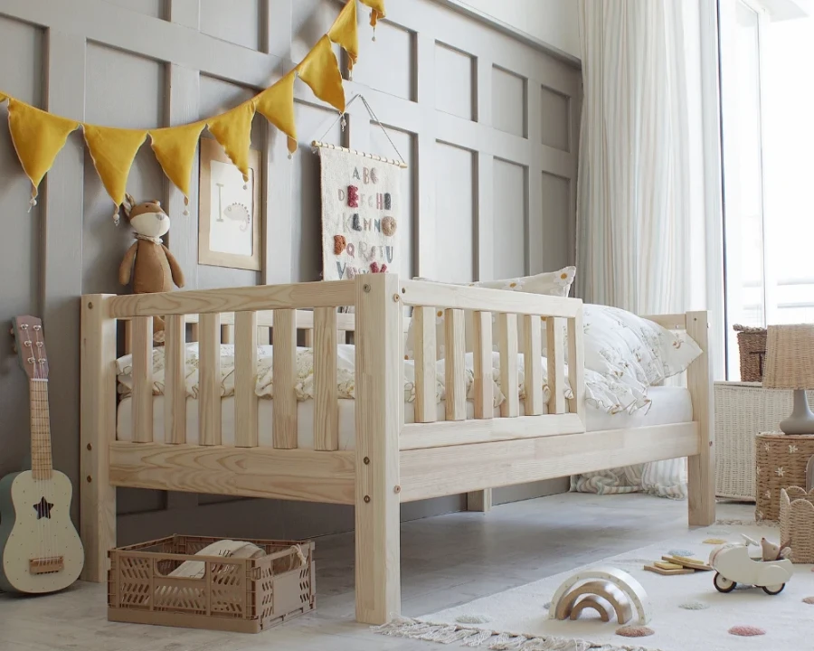 Gemütliches Kinderbett aus Massivholz mit Rausfallschutz in einem hellen Kinderzimmer.