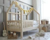 Hausbett aus Naturholz für Kinder mit gelber Wimpelkette und Rausfallschutz.