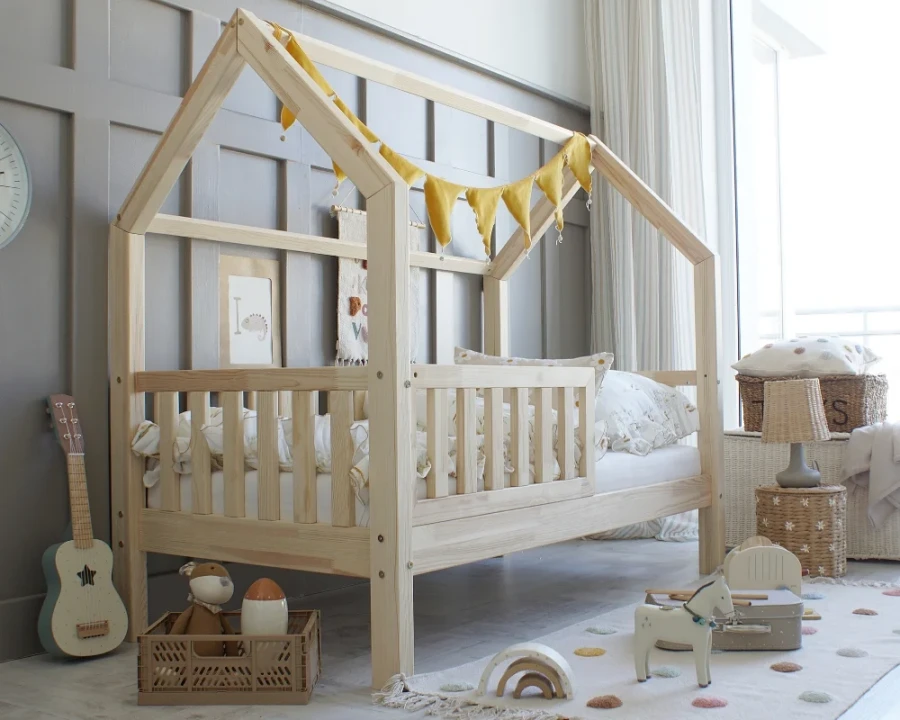 Hausbett aus Naturholz für Kinder mit gelber Wimpelkette und Rausfallschutz.