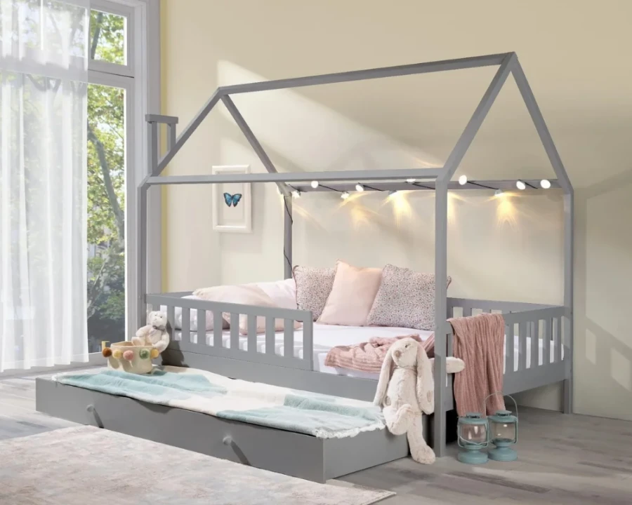 Gemütliches graues Kinder-Hausbett mit Lichterkette, Kissen und Kuscheltieren im hellen Zimmer.