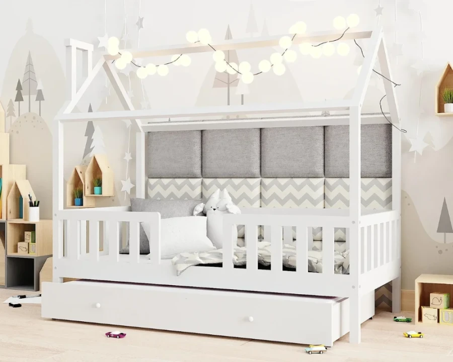 Weißes Kinder-Hausbett mit gepolstertem Kopfteil, Lichterkette und Dekoration im Spielzimmer.