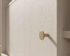 Detailaufnahme eines goldenen Möbelknopfes an einer beigen Schrankfront mit Holzstruktur.