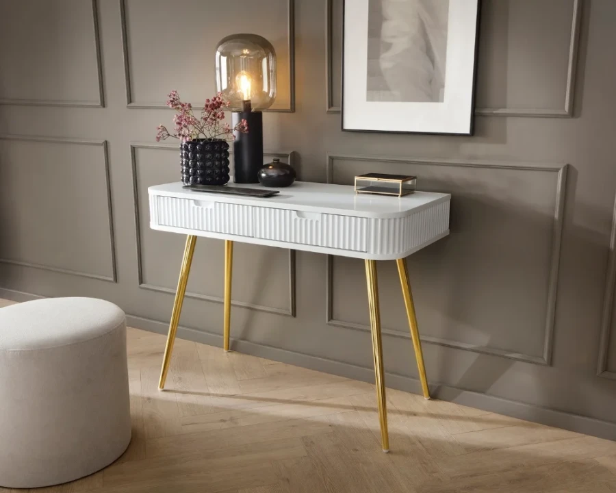 Eleganter weißer Konsolentisch mit goldenen Beinen vor einer grauen Wand mit Zierleisten.