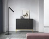 Moderne schwarze Kommode mit goldenen Beinen und geriffelter Front im Wohnzimmer-Ambiente.