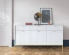 Weißes Sideboard mit Rillen-Design und goldenen Metallfüßen auf Parkettboden.