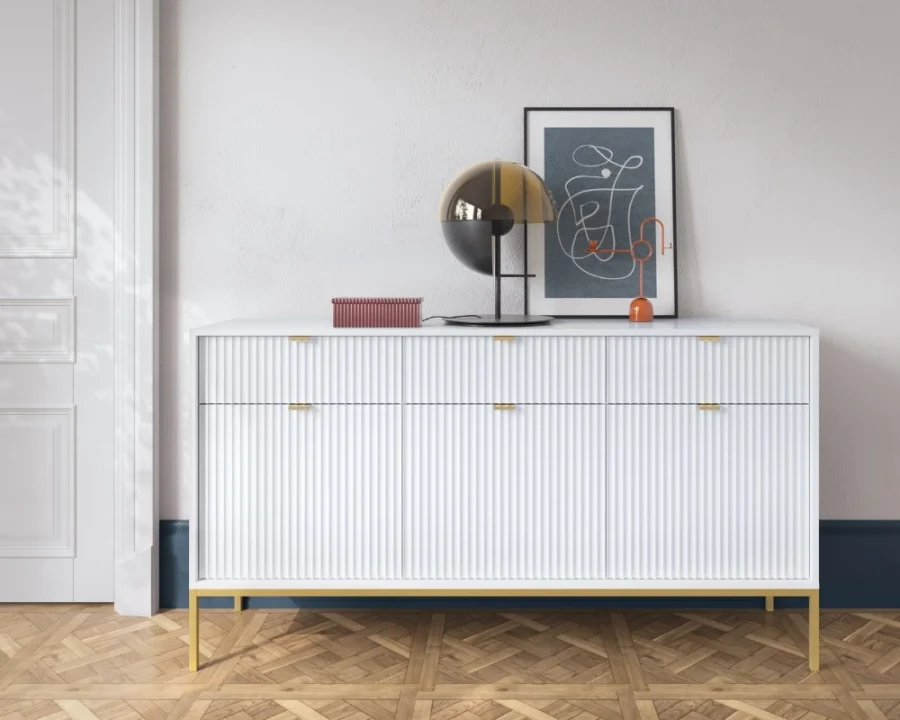 Weißes Sideboard mit Rillen-Design und goldenen Metallfüßen auf Parkettboden.