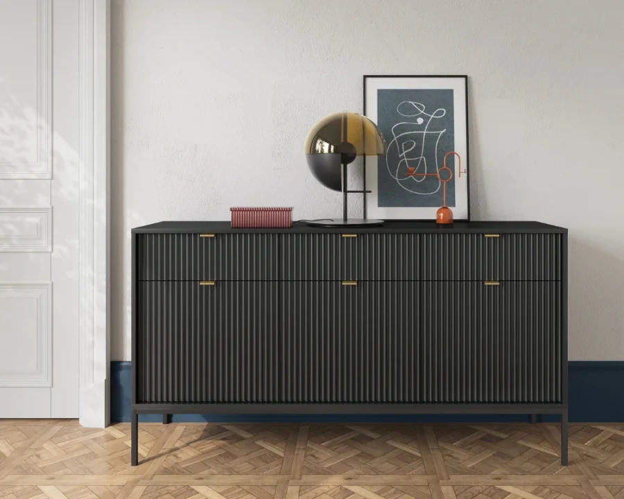 Schwarzes Sideboard mit Rillenstruktur und schwarzen Beinen vor einer hellen Wand.