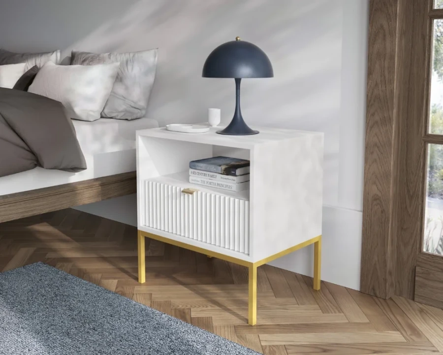 Weißer Nachttisch mit goldenen Beinen, geriffelter Schublade und offenem Fach neben einem Bett.